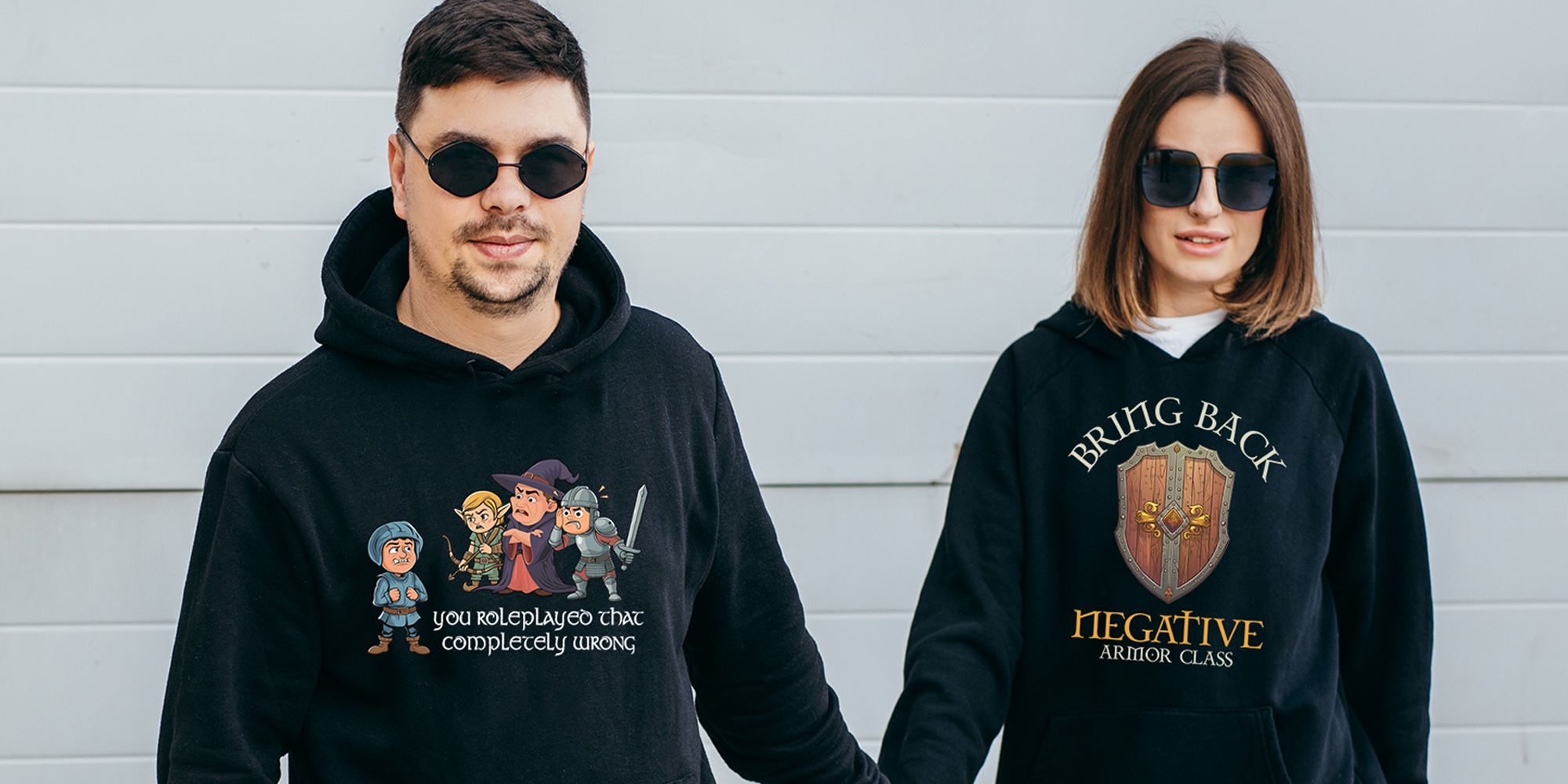 Man and woman in sunglasses and holding hands while wearing black hooded sweatshirt with TTRPG-themed sayings and artwork.